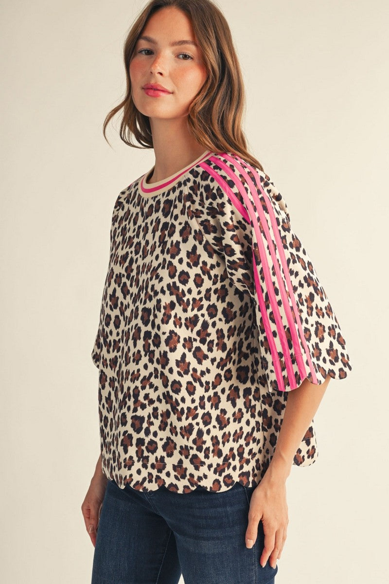 A woman wearing a leopard print top with bright pink shoulder straps and blue jeans, photographed against a plain light beige studio background.