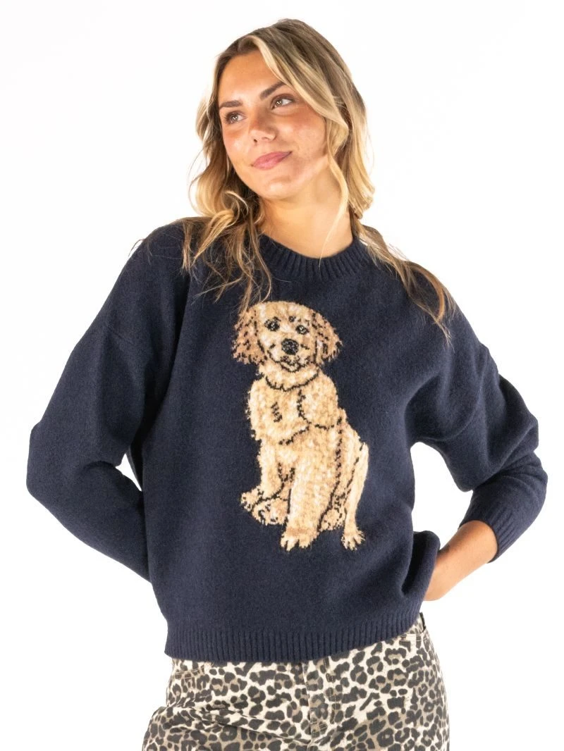 A woman wearing a navy blue knit sweater with a large beige and brown dog graphic on the front, paired with leopard print pants, against a plain white background.