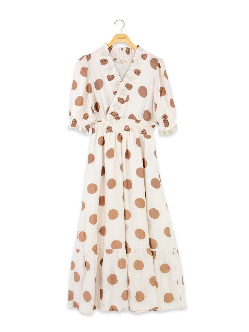 An off-white wrap-style midi dress with brown polka dots, featuring short puff sleeves, a ruffled collar, and a tiered skirt, hanging on a wooden hanger against a white background.