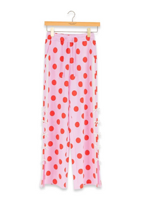 Pink wide-leg pants with a red polka dot pattern, hanging on a wooden hanger against a white background.