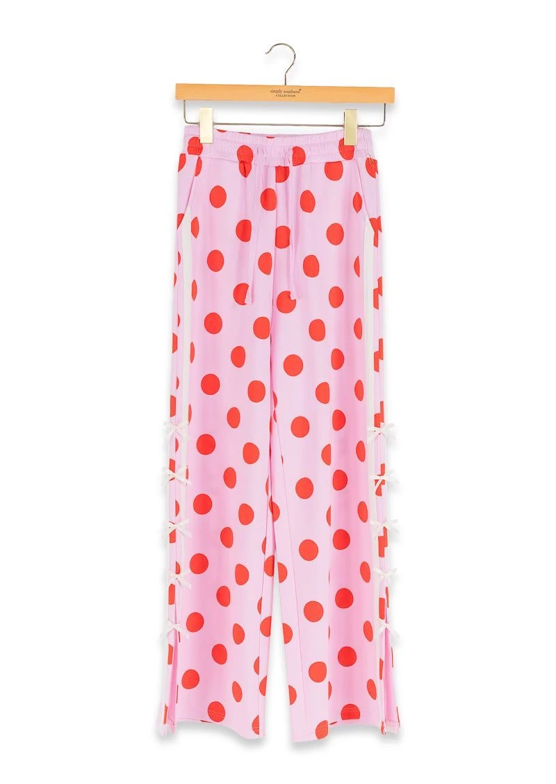 Pink wide-leg pants with a red polka dot pattern, hanging on a wooden hanger against a white background.