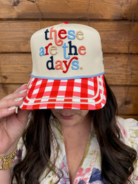 Person wearing a cap with 'these are the days' text and red checkered brim against a wooden background