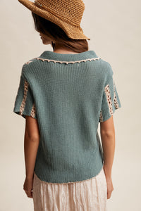 Woman wearing a teal knitted top with lace details and a straw hat on a neutral background