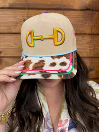 Beige cap with colorful design and leopard print visor held by a person against a wooden background