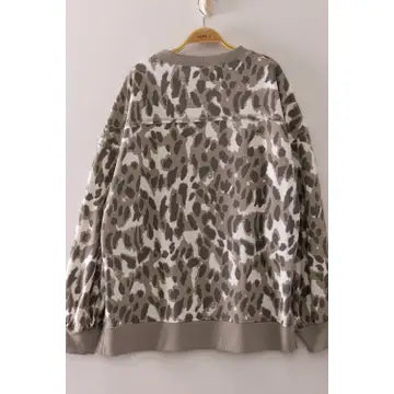 A long-sleeve crewneck sweatshirt with an oversized leopard print pattern in gray, brown, and beige, hanging on a wooden hanger against a plain light gray wall.