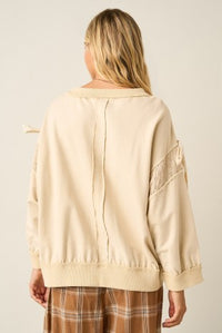 A woman shown from the back wearing a cream-colored knit sweater with lace sleeve details and a tie at the collar, paired with brown plaid pants, against a plain light beige background.