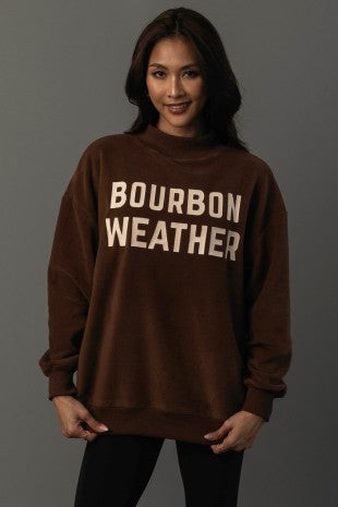 Woman wearing a brown sweatshirt with 'Bourbon Weather' text on a gray background