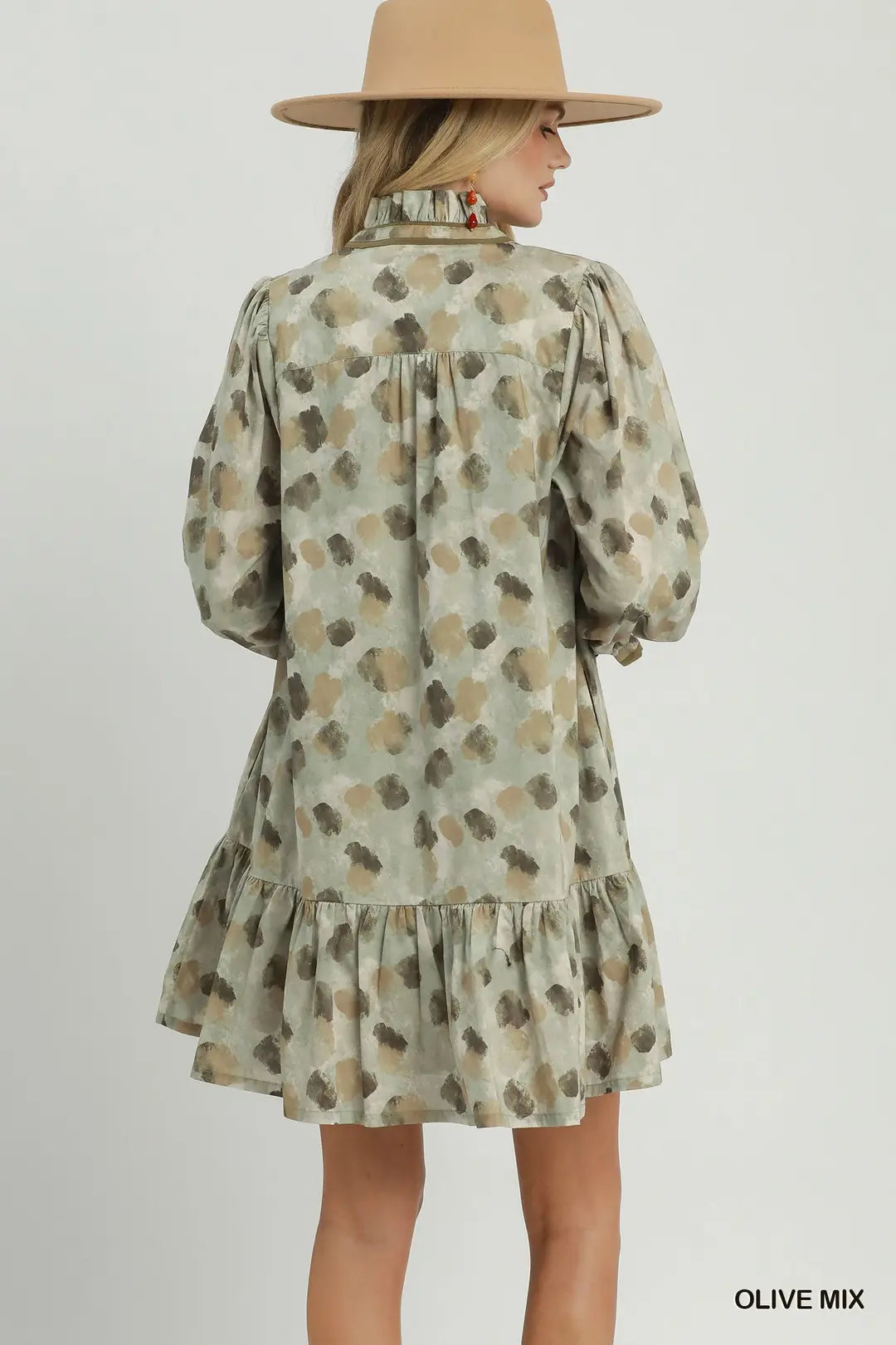 A woman shown from the back wearing a short olive green dress with a brown and beige abstract spotted pattern, long puff sleeves, and a ruffled hem. She is also wearing a wide-brimmed tan hat.