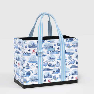 A tote bag with a blue and white illustrated pattern of London landmarks and street scenes, featuring light blue and white striped handles and a black base, shown on a light gray background.
