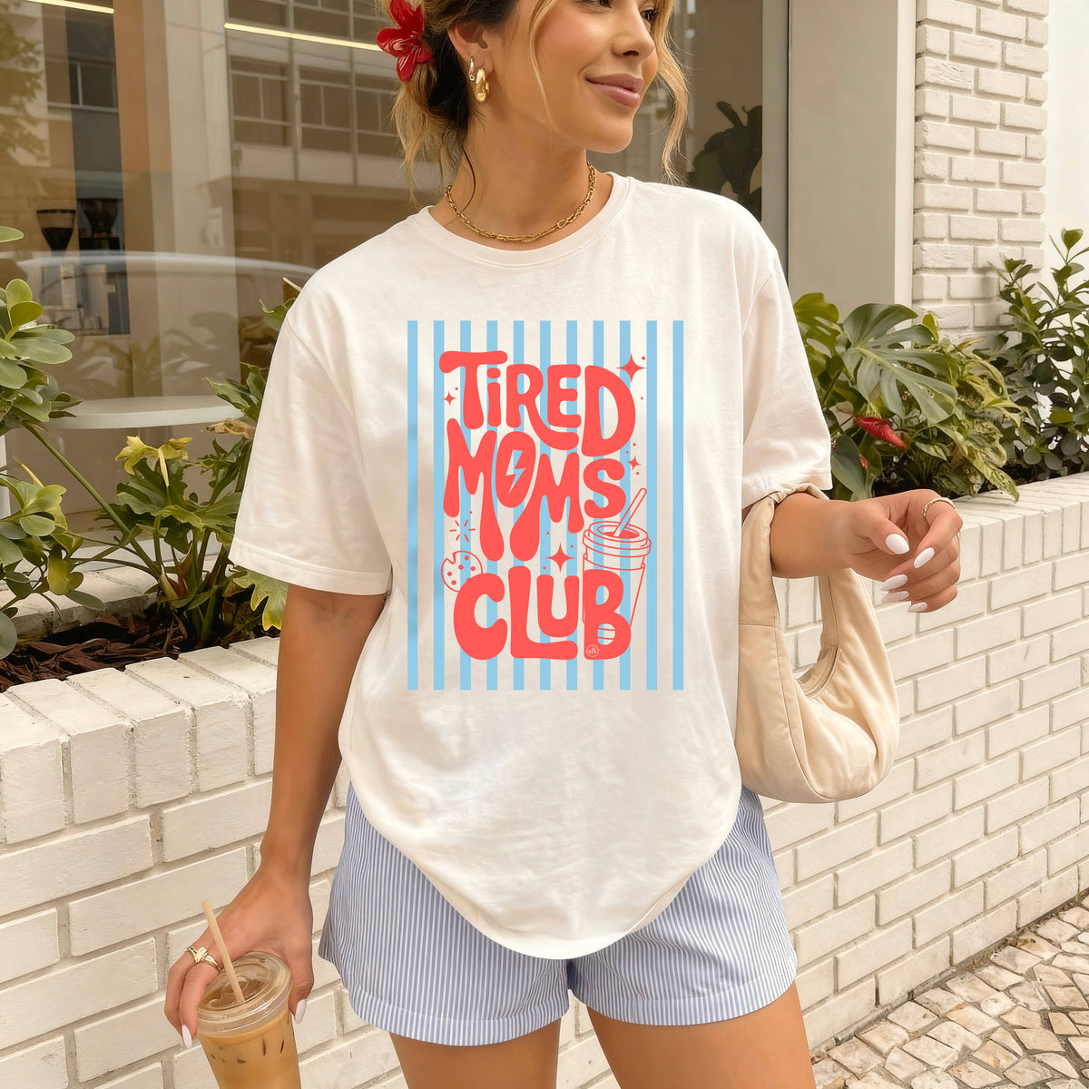 Woman wearing a 'Tired Moms Club' t-shirt outdoors.